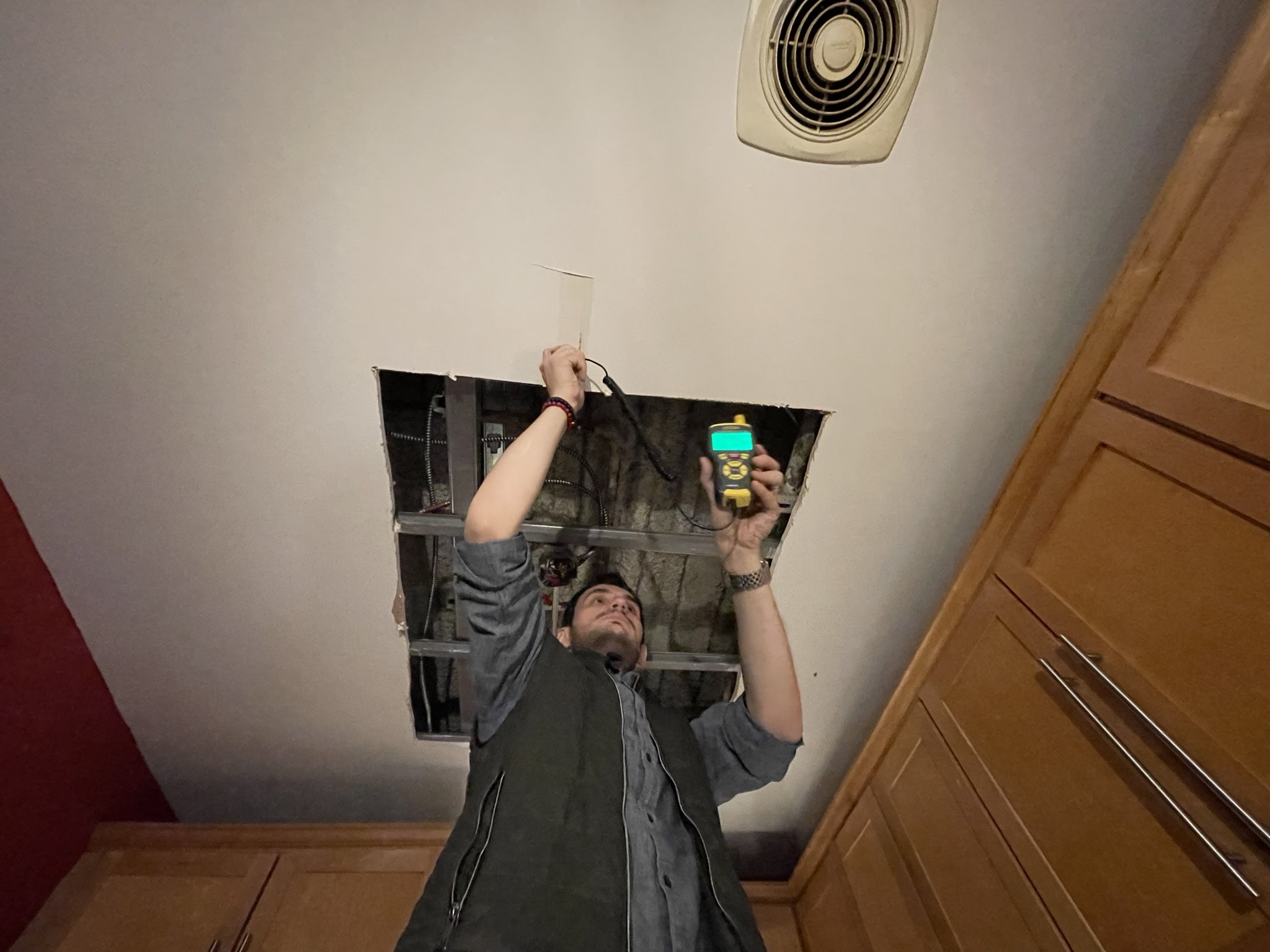 Technician inspecting an opened ceiling cavity with a moisture meter