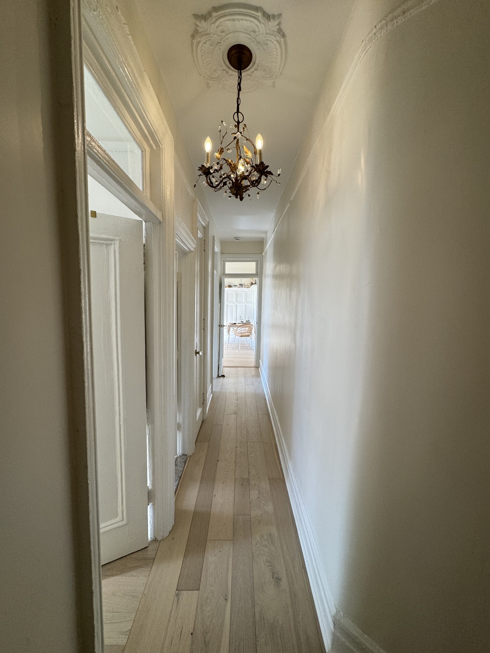 Completed hallway with restored trim, chandelier and light wood flooring