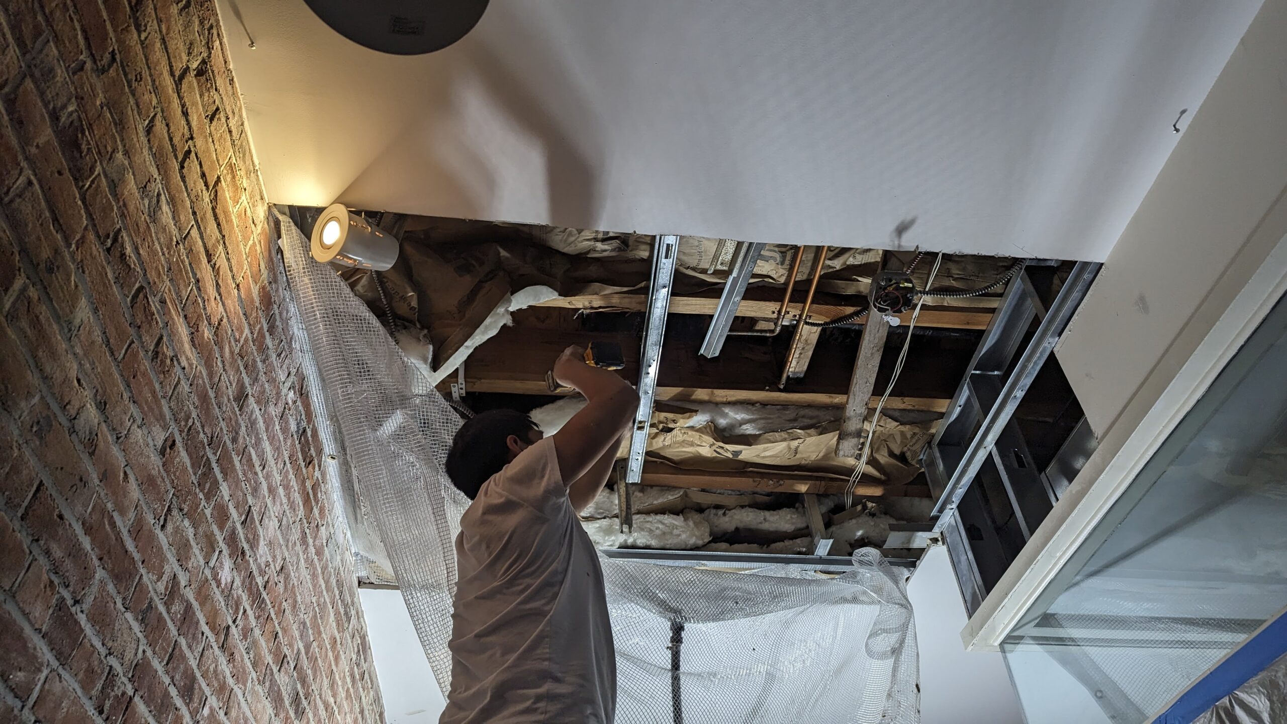 Technician working beneath an opened ceiling beside a historic exposed-brick wall
