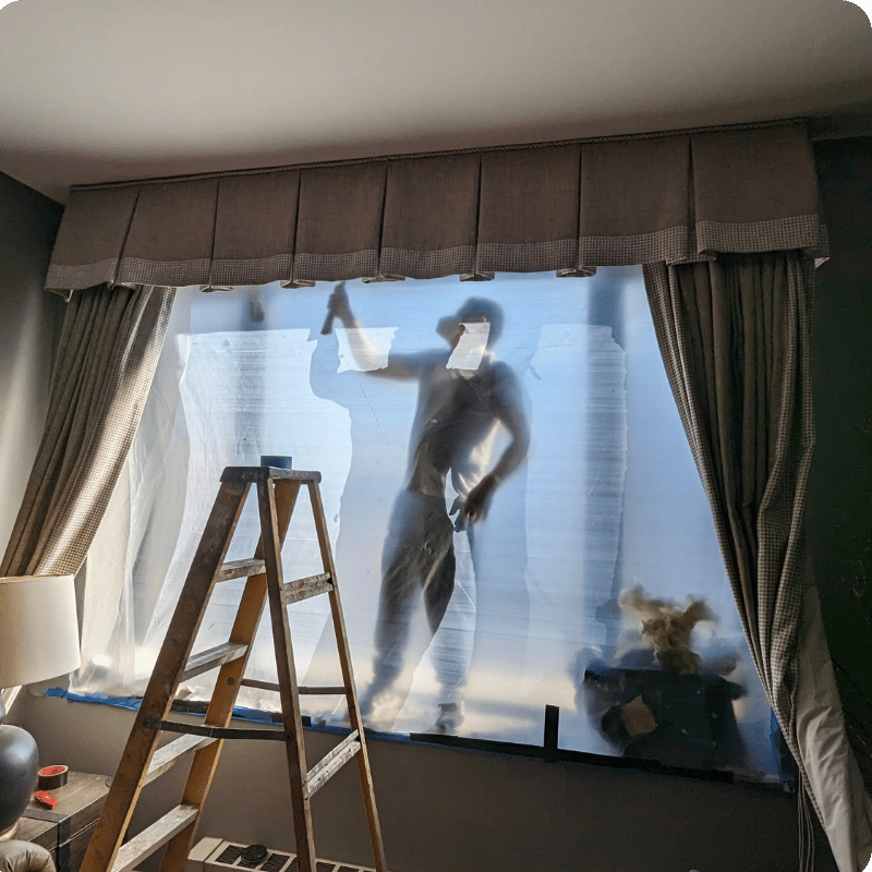 Window and curtains fully wrapped in protective plastic sheeting during renovation work